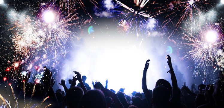 Stage lights and crowd of audience with hands raised at a music festival. Fans enjoying the party vibes. New Years Eve concept.