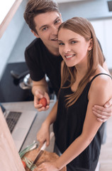 happy young couple standing near the kitchen table and looking at the camera