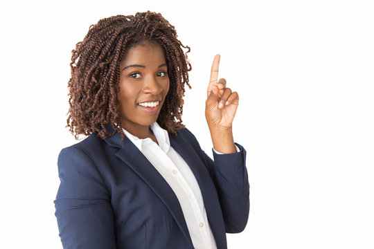 Joyful young professional having new idea, pointing index finger up. African American business woman standing isolated over white background, looking at camera, smiling. Advertising concept