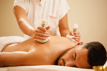 Obraz na płótnie Canvas Relaxed man receiving Thai herbal compress massage at the spa.