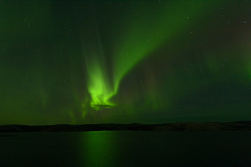 Northern lights over the lake and hills. Aurora at night in the sky in the north.