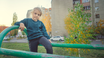Fototapeta na wymiar A charming little girl in casual clothes sits on a metal structure in the yard.