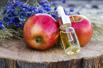 Glass bottle of apple essential oil near fresh apples on a wooden table. Essential oil is used to...