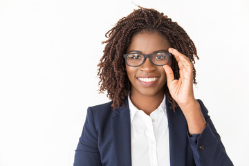 Happy satisfied customer trying on glasses. Young African American business woman touching eyewear, looking at camera. Isolated front over white background Eyesight concept