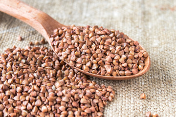 Uncooked buckwheat in a spoon on burlap background. Buckwheat is used for cooking.