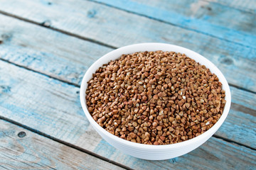 Uncooked buckwheat in a bowl on old blue boards. Buckwheat is used for cooking.