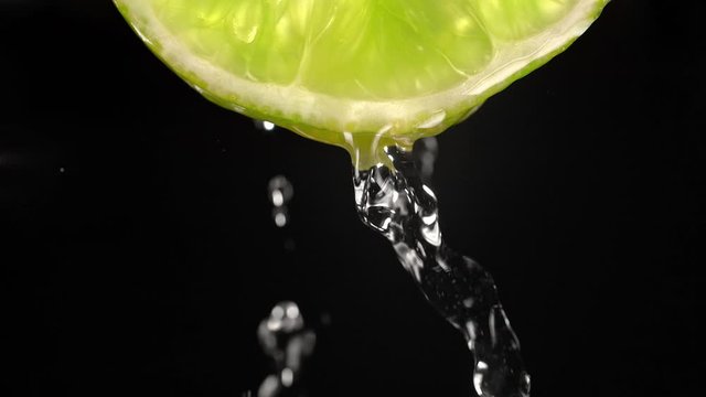 Macro shot of Water Flowing Down the Backlit Juicy, Fresh, Raw Lime Slice on the Black Background. Healthy Citrus Vegetarian Diet. Shot in 1000 FPS with High Speed Camera, Phantom Flex 4K