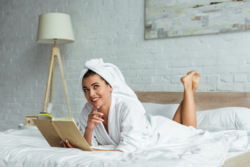 attractive woman in towel and bathrobe holding book at morning
