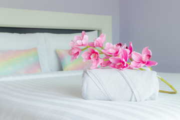flowers and white bath towel roll on bed at hotel bedroom