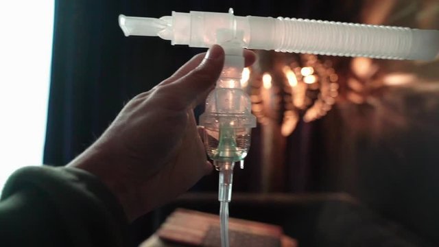 One hand holding Nebulizer assembly with liquid medication in nebulizer chamber. Breathing treatment preparation.