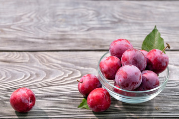 Ripe plums and leaves in glass bowl on wooden table
