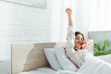 attractive woman with closed eyes stretching herself at morning