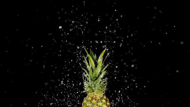 Water Jet pushing up the Majestic Ripe Tropical Pineapple Fruit to the Top of the Black Background. Sparkling Water Drops Splashing around. Shot in 1000 FPS with High Speed Camera, Phantom Flex 4K