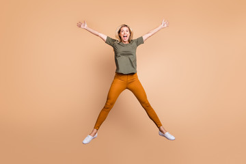 Full length photo of crazy funky lady jumping high making star shape figure spending best free time wear green t-shirt yellow trousers sneakers isolated beige color background