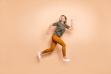 Fototapeta na wymiar Full body profile photo of crazy lady jumping high speed race marathon participant competitive mood rushing to finish wear green t-shirt yellow trousers isolated beige color background