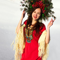 young stylish brunette girl in red dress with crown of christmas trees and berries on the head is...