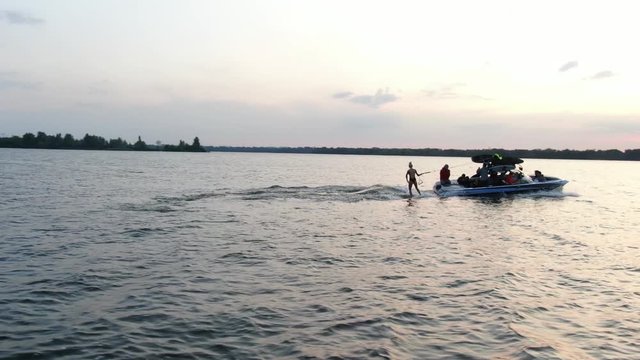 Young woman starts wake surfing on the river at sunset, aerial footage