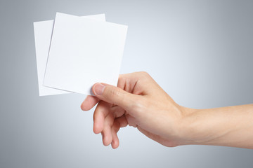 Obraz premium Male hand holding two square blank sheets of paper (tickets, flyers, invitations, coupons, etc.) on gray background