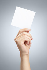 Male hand holding a square blank sheet of paper (ticket, flyer, invitation, coupon, etc.) on gray background