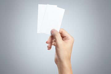 Hand holding two small pieces of paper or plastic (cards, tickets, flyers, invitations, coupons, banknotes, etc.) on gray background