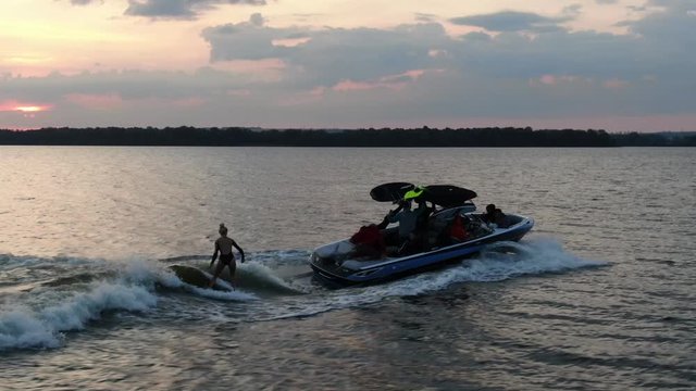 Aerial footage of a young woman wake surfing without the rope, riding the wave