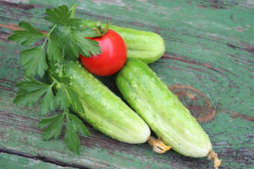 Organic green cucumbers and tomato on the background of boards
