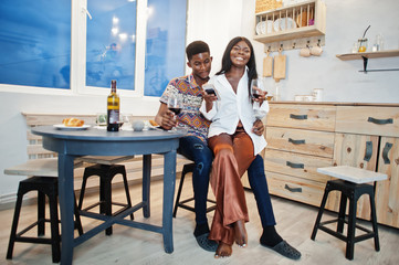 Fototapeta na wymiar Afro american couple sweethearts drinking wine in kitchen at their romantic date with mobile phone at hands.