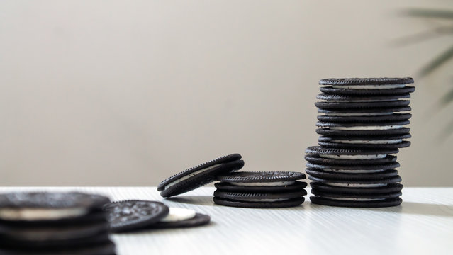 black cookies standing pinnacle with white cream center on a white wooden background with palm leaves behind.