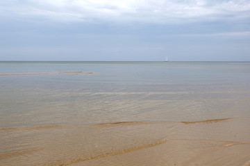 Sandy shoal of the cold Baltic Sea with cloudy weather on empty beach and alone yacht in drift on skyline