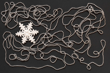 Holiday background , white snowflake and silver decorative beads on black background, flat lay, top view