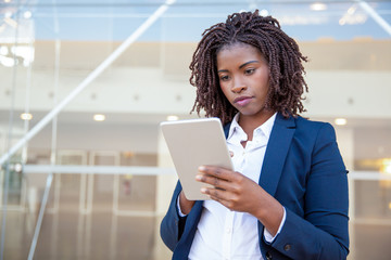 Focused professional using app on tablet outside. Young African American business woman holding...
