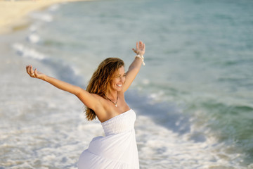 Young happy woman having fun while standing by the sea with her arms outstretched.