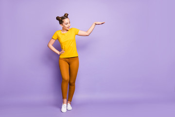 Fototapeta na wymiar Full body photo of pretty teenager lady holding arm air showing big size length of new promoted product wear yellow t-shirt trousers isolated pastel purple background