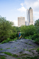 Frau mir Fahrrad im Central Park auf Stein mit Blick auf Hochhäuser 