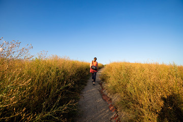 Frau l&auml;uft durch dicht bewachsenes Gras auf Feld im Sonnenuntergang