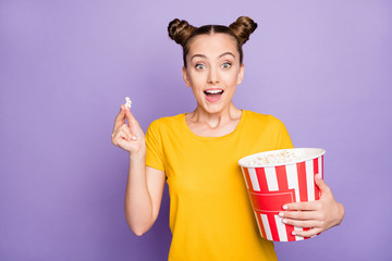 Photo of brunette white trendy cheerful millennial watching movie excited about unexpected events in plot holidng bucket of pop corn expressing amazed emotions isolated violet pastel color background