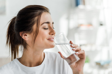 Fototapeta smiling girl holding drinking water from glass in the morning obraz