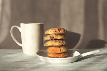 Freshly baked homemade cookies on white plat with cup of tea or coffee. Beautiful natural light and shadows. Light gray background.