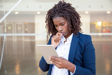 Pensive professional reading on screen outside. Young African American business woman using tablet,...
