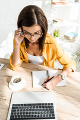 beautiful confident freelancer with coffee cup working with laptop and notebook in home office