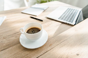 close up of coffee cup and laptop on table in light office