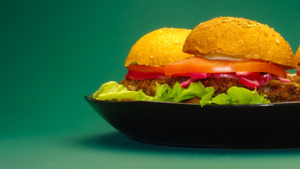 Homemade hamburgers on black plate on uniform green background