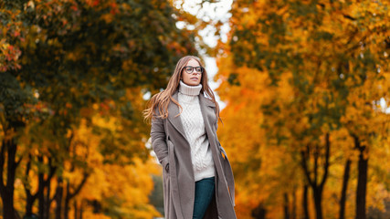 Pretty stylish young hipster woman in a fashionable knitted sweater in an elegant long coat in...