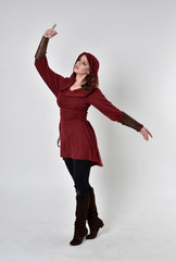 full length portrait of a brunette girl wearing a red fantasy tunic with hood. Standing pose on a white studio background