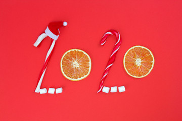 Happy New Year 2020 concept. Text from candy canes, marshmallows, Santa't hat, dried oranges on red...