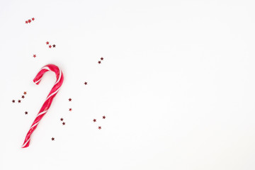 Candy cane, little red stars confetti on white background. Merry Christmas, Happy New Year concept. Top view, flat lay, copy space