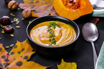 pumpkin cream soup with dark bread croutons and seeds with autumn leaves decoration on black background