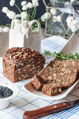 Freshly baked rye bread with seeds and raisins on sourdough without yeast on a white plate with a knife for cutting and black salt. Homemade cake