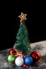 Christmas tree miniature decorated with colorful balls and shining star isolated on dark background. Concept of merry christmas, holidays, happy new year, gifts, happiness and celebration.