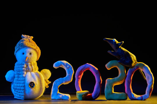 2020 New year design concept. Colored plasticine figures on a black background with mixed light, rat and snowman